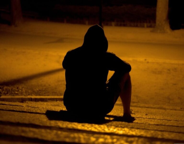 Silhouette of a person in a hoodie sitting alone at night under a streetlight