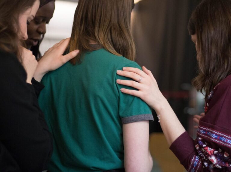 Three women laying hands on a fourth while praying for her