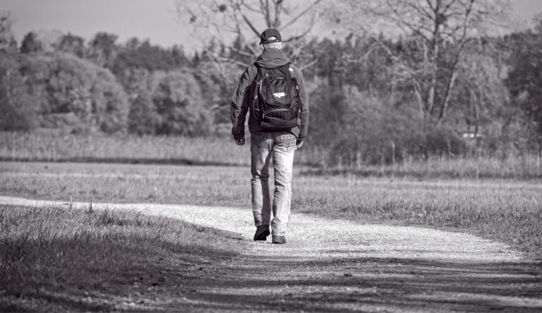 Man wearing hat and backpack walking alone along road in the wilderness