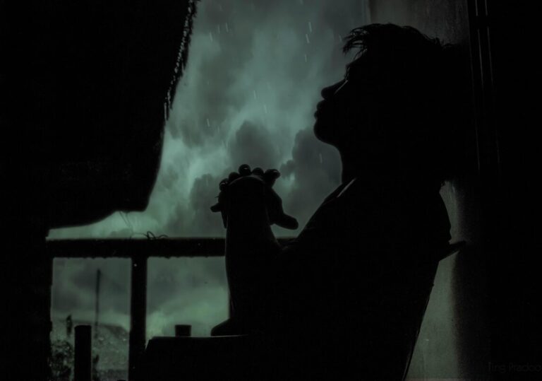 Young man's silhouete against the window of a dark, stormy sky