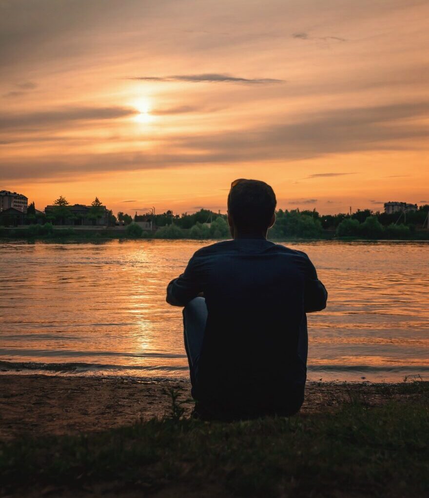 Man sitting by lake at sunset